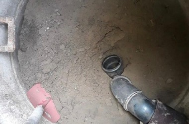 Ein beschädigtes Abwasserrohr in einem Erdloch, umgeben von Schmutz und Erde. Ein weiteres Rohrstück liegt daneben.